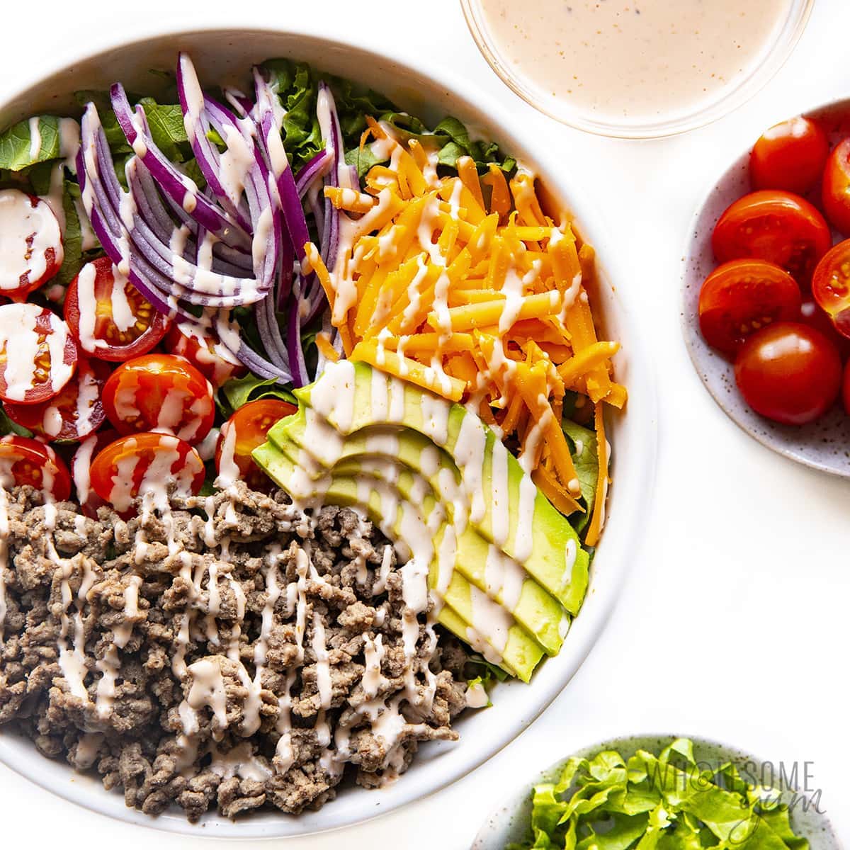 Keto loaded burger in a bowl with a bowl of sauce, tomatoes, and lettuce.