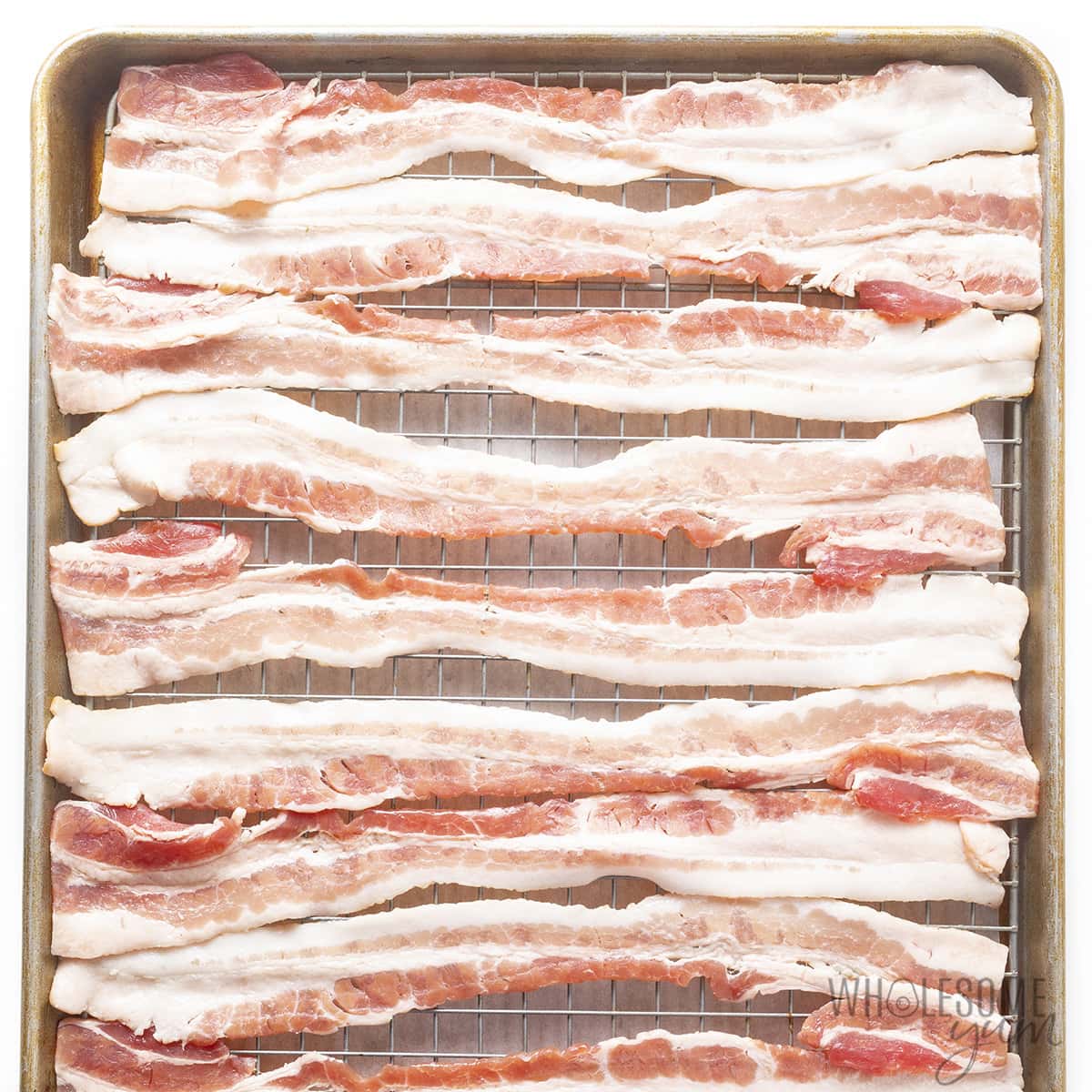 Raw bacon on a rack over a baking sheet.