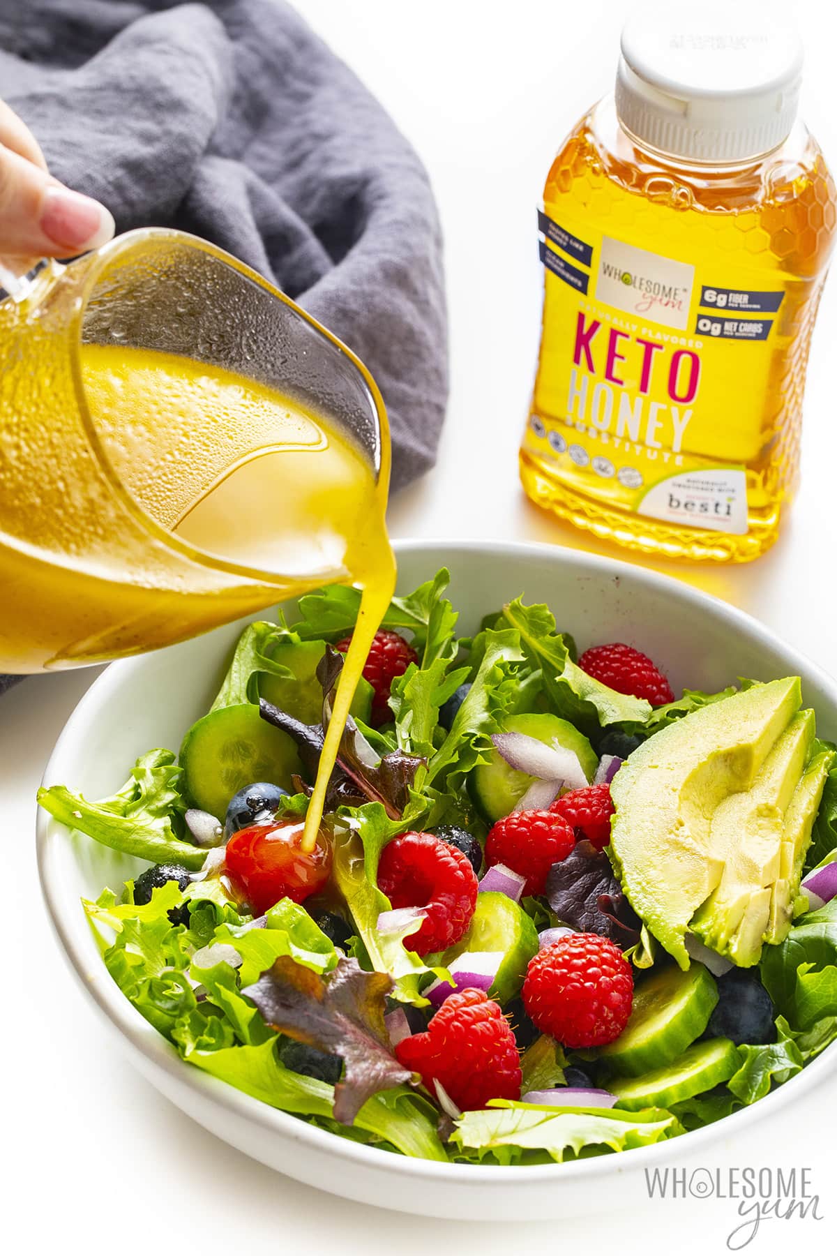 Pouring keto salad dressing over salad.