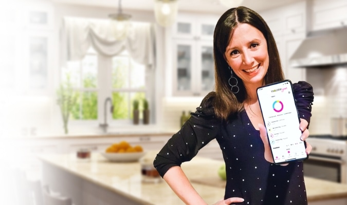 Maya holding phone displaying Wholesome Yum app.
